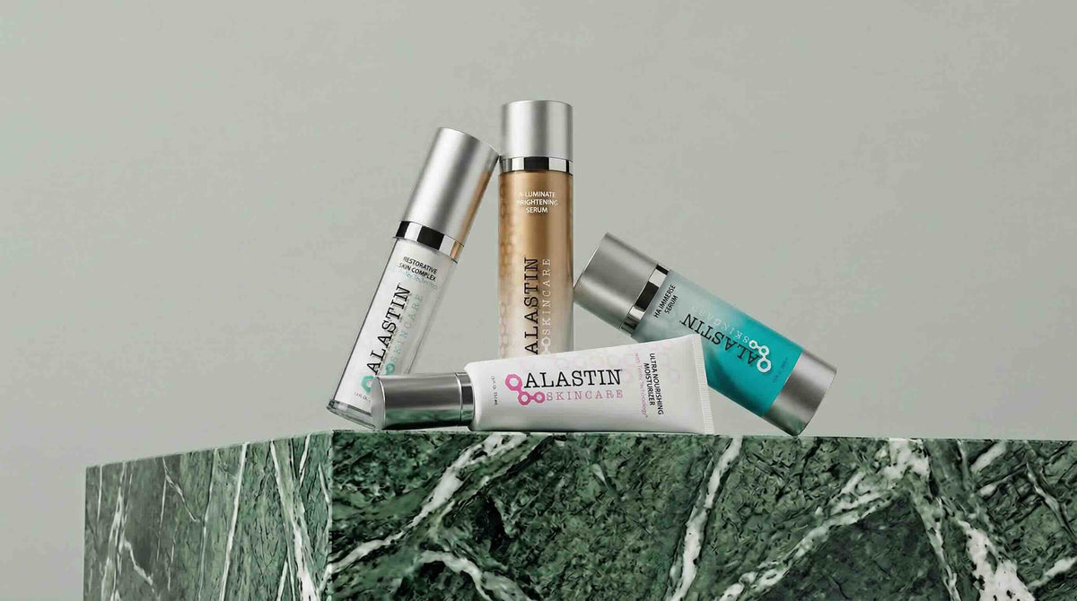 Collection of Alastin skincare products on a marble surface with a gray background