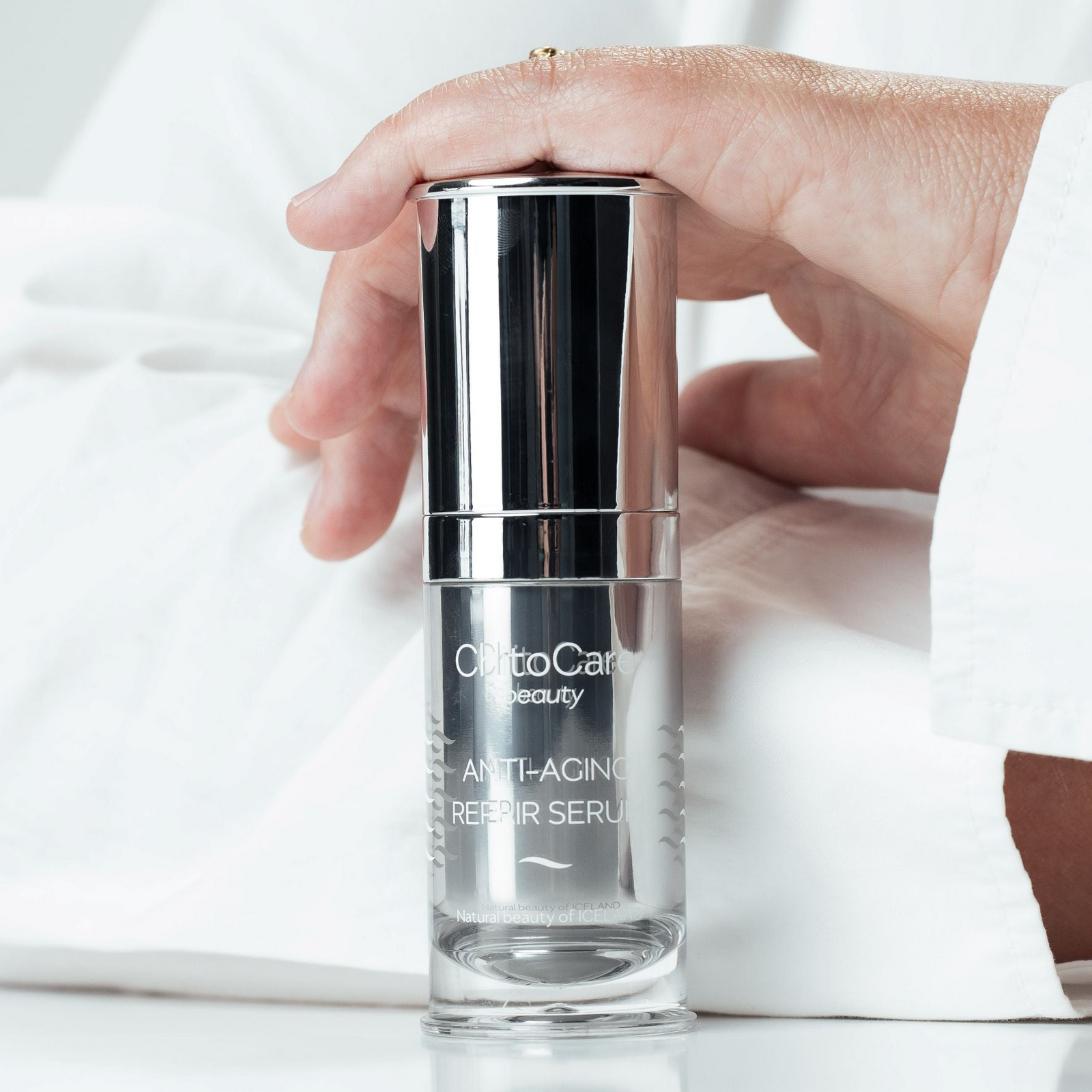 A hand holding a clear cosmetic serum bottle with a reflective silver cap. The bottle is labeled 'CHITOCARE beauty' and 'ANTI-AGEING REPAIR SERUM'.