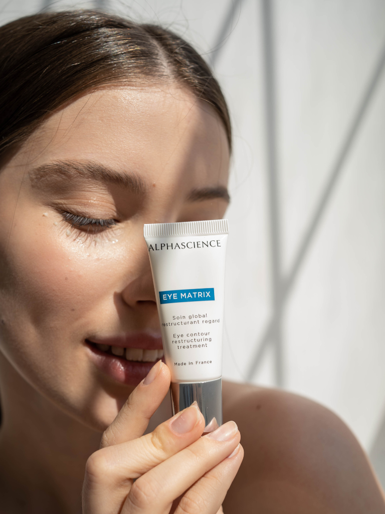 Model holding a tube of Alphascience Eye Matrix skincare product against a neutral background