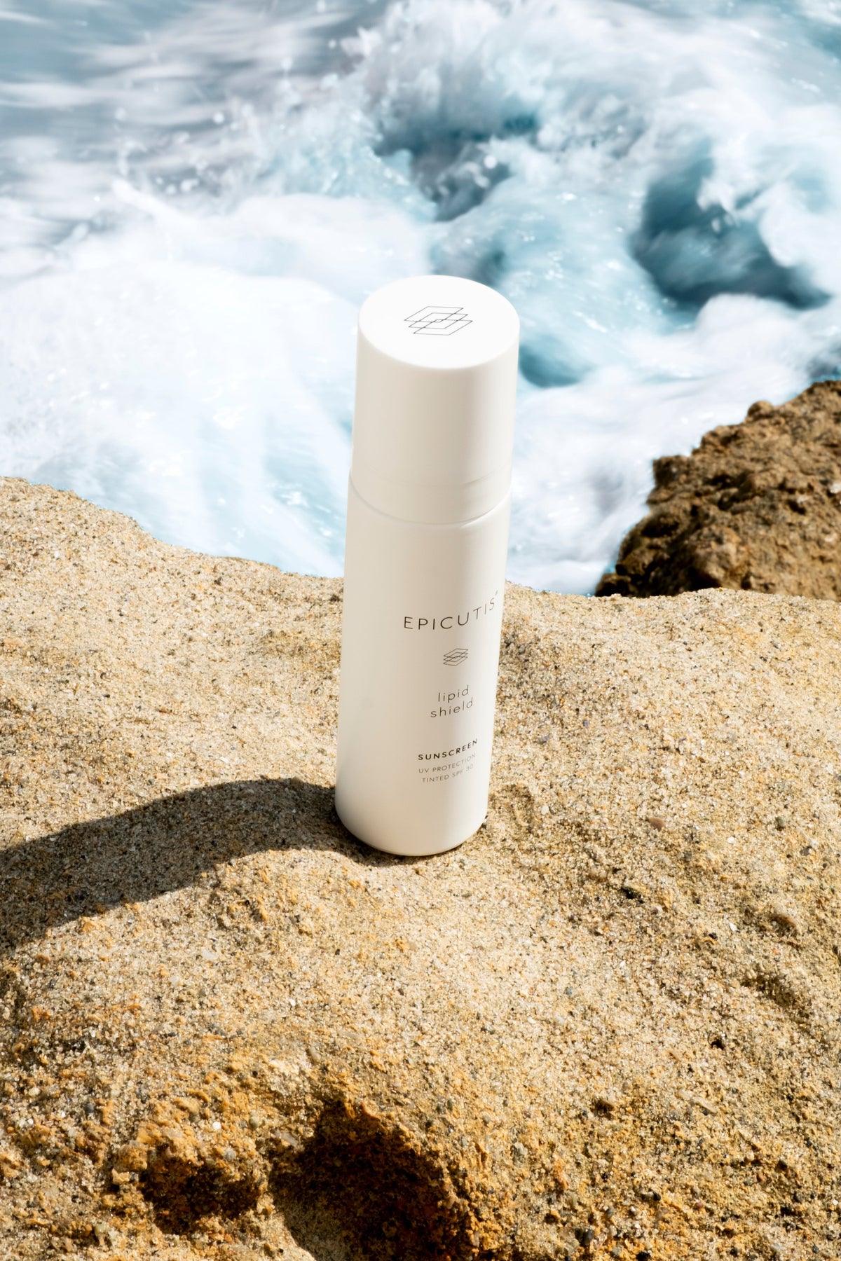 White bottle labeled 'Epicutis' on a rocky surface with ocean waves in the background