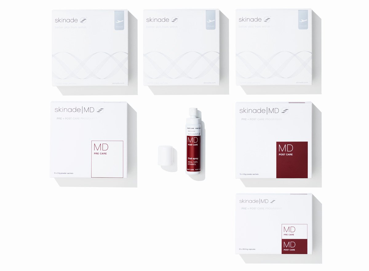 Skinade MD nutritional protocol designed to support healing, collagen production, and post-procedure recovery. Six skincare product boxes and one bottle from skinade|MD are arranged on a clean white background. The packaging is predominantly white with subtle gray wave graphics and one box featuring a dark red square with 'MD' text.
