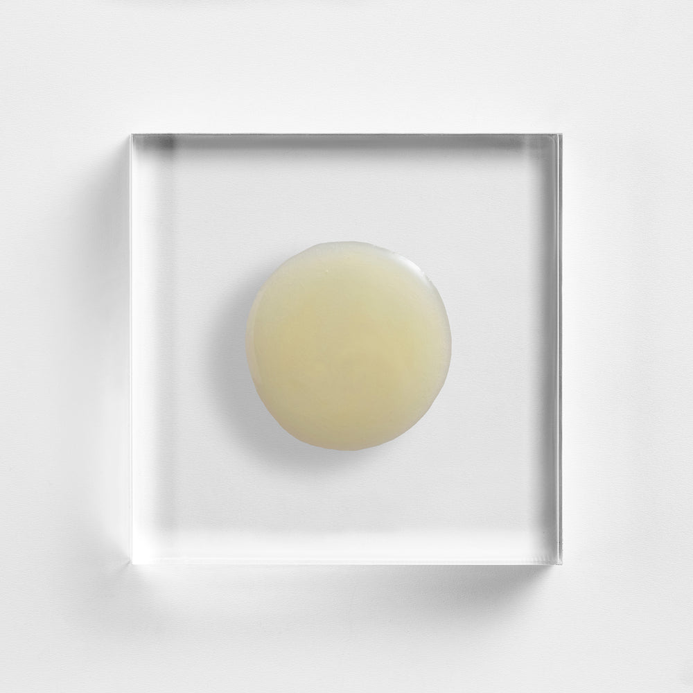 Round beige object in a clear square frame on a light gray background. Close-up texture of NEOVA Cell Renewal Serum, alpha-beta-retinol serum with glycolic acid, lactic acid and salicylic acid.