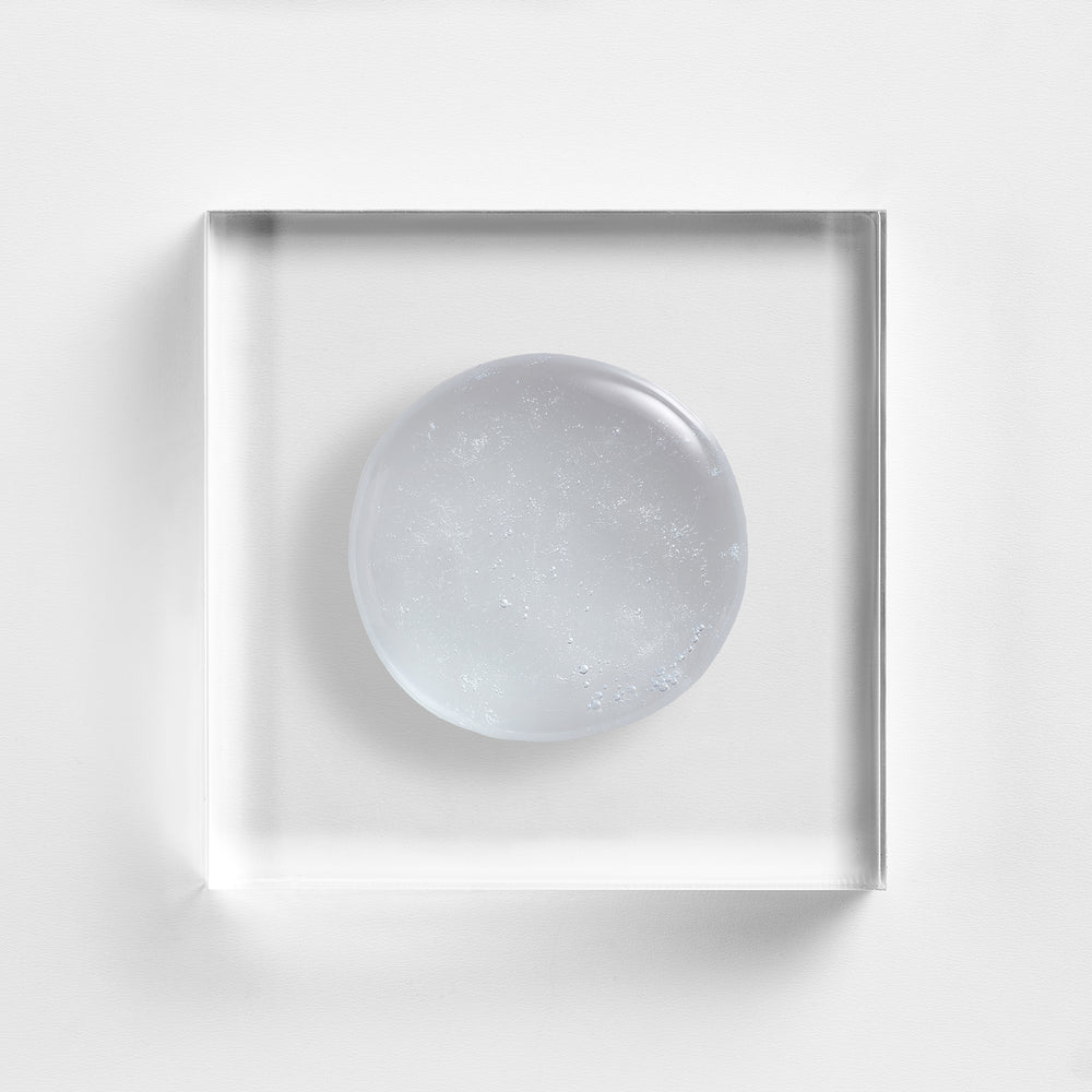 A clear square acrylic block with a smooth, circular transparent white center, photographed from above on a clean white background. Close up of Cu3 Gentle Cleanser by Neova.