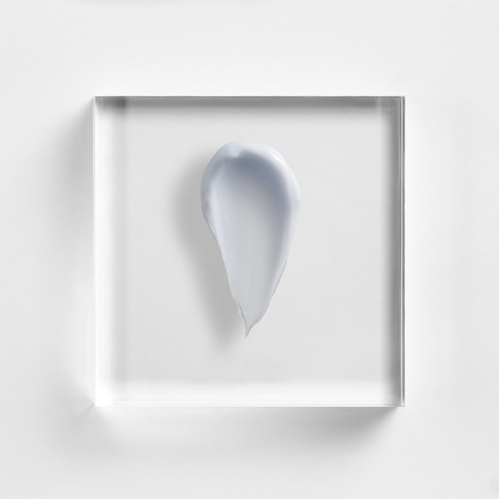 A small smear of pale blue-gray cream or gel centered inside a clear square acrylic block, photographed on a clean white background. Close-up of NEOVA Cu3 Tissue Repair’s rich occlusive cream texture for hydration and skin comfort.