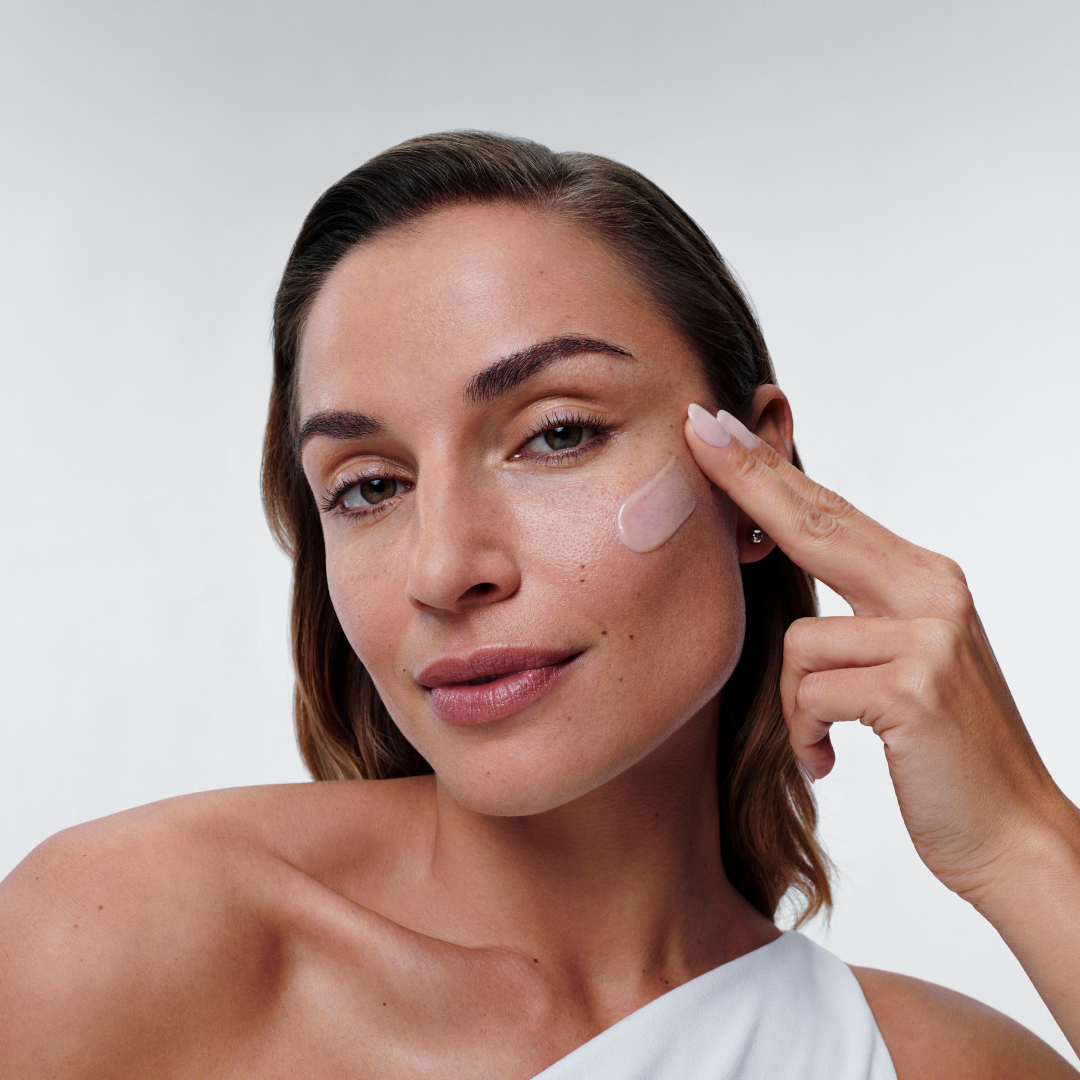 Woman applying Alastin Restorative Skin Complex to cheeks, targeting fine lines, firmness and uneven tone.