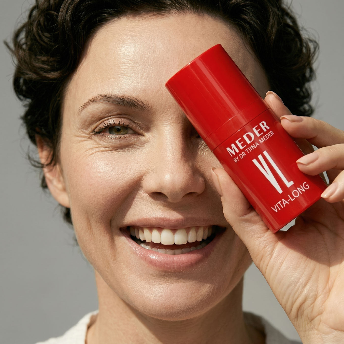 Woman holding a red skincare product labeled 'MEDER Vita-Long' against her face.
