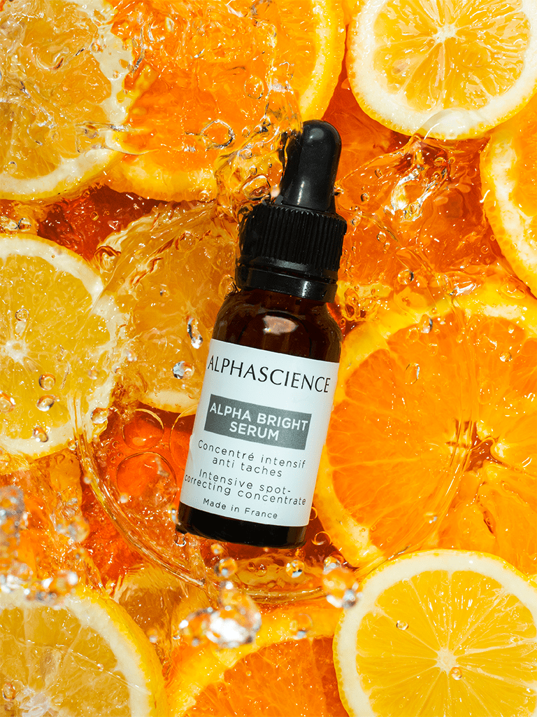 Alpha Bright Serum bottle from AlphaScience with dropper on a background of sliced oranges and lemons.