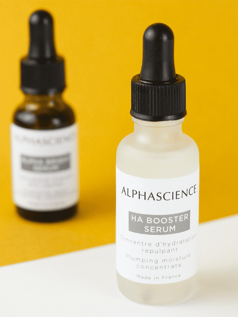 Two bottles of Alphascience HA Booster Serum on a yellow background