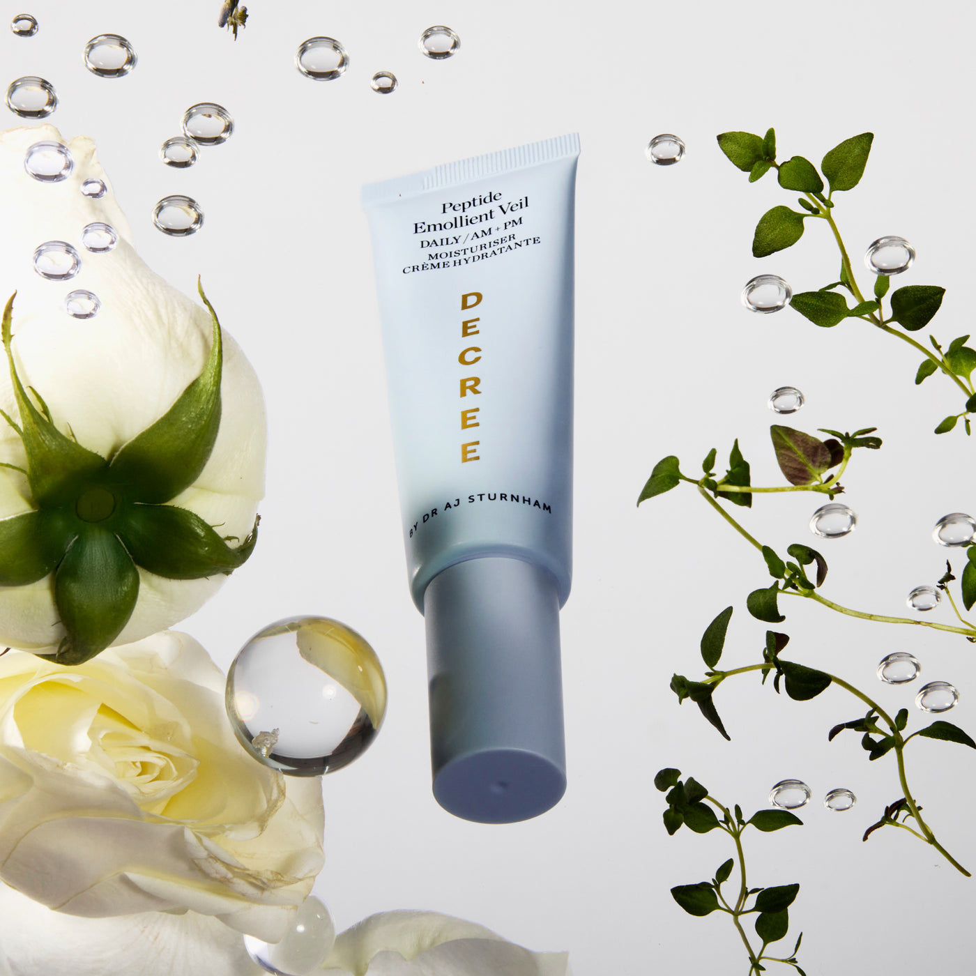Skincare tube labeled 'DECREE' with flowers and water droplets on a light background. Decree Peptide Emollient Veil cream texture enriched with peptides, safflower seed oil, and squalane.