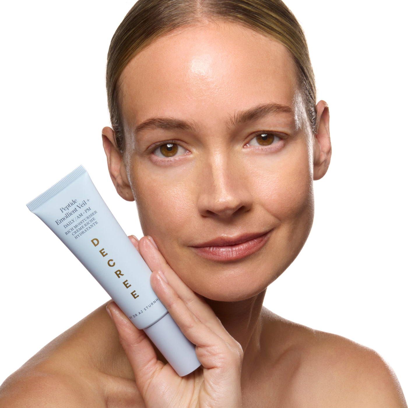Decree Peptide Emollient Veil+ for deeply hydrated, softer, smoother, firmer, and more radiant-looking skin. Woman holding a skincare product with a plain background