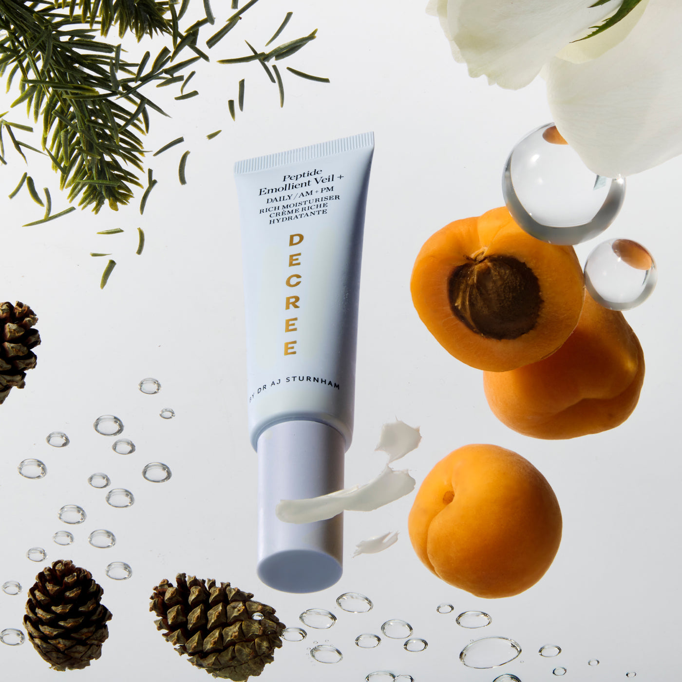 Tube of Decree skincare product with apricots, pinecones, and flowers on a light background. Decree Peptide Emollient Veil+ rich cream texture with peptides, botanical oils, and nourishing emollients.