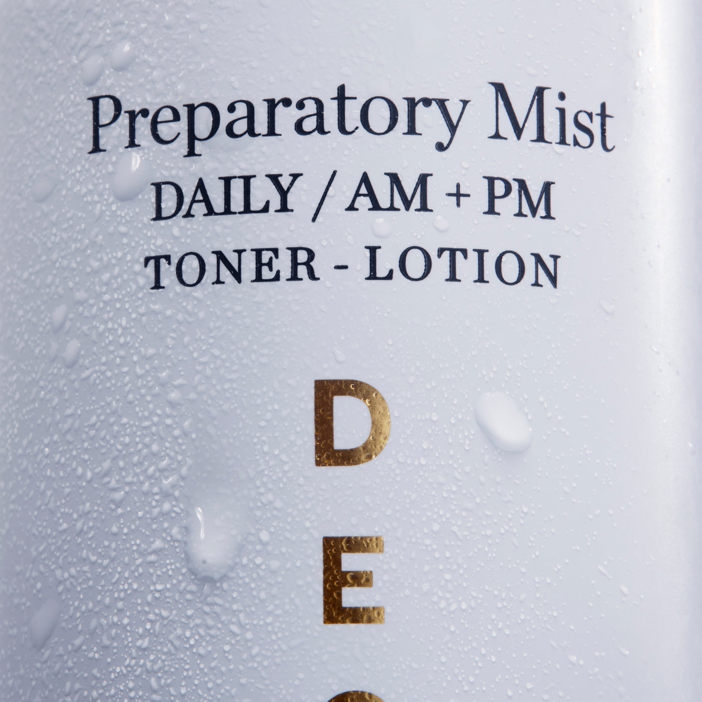 Close-up of a white bottle labeled 'Preparatory Mist DAILY / AM + PM TONER - LOTION' with water droplets on the surface and gold lettering.