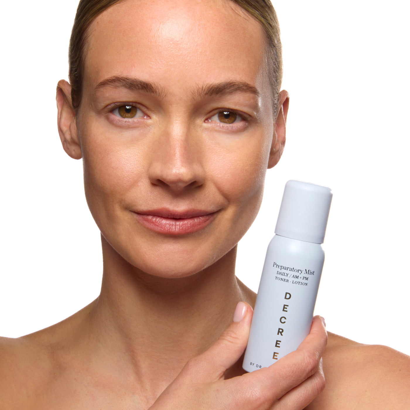 Woman holding a DEGREE product with a plain background. Decree Preparatory Mist 75 ml packaging for calming, plumping, and preparing the skin after cleansing.