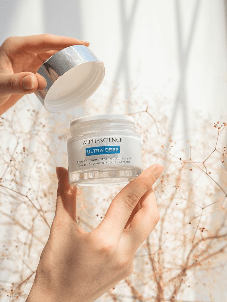 Person holding a skincare product with Alphascience Ultra Deep against a soft, blurred background.