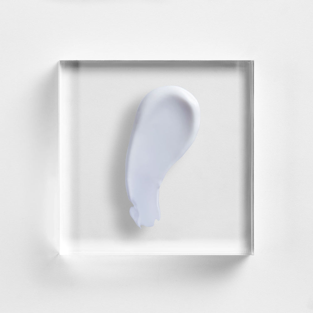 A translucent square acrylic block displaying a smooth, pale lavender-gray cream swatch on a clean white background. Close-up of NEOVA Body Repair lotion texture, restorative body care for smoother, softer, more resilient-looking skin.