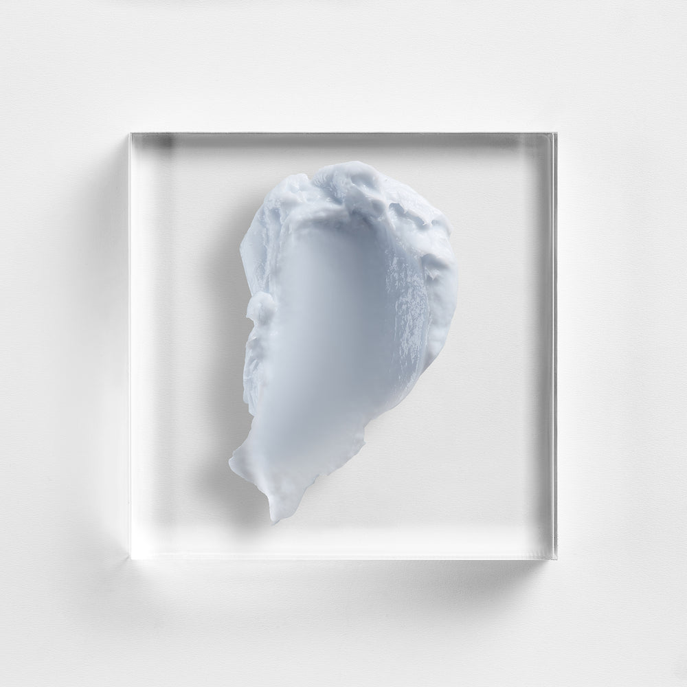 A square clear acrylic block containing a sculptural, organic pale blue-gray form, photographed against a clean white background. Close-up texture of NEOVA Night Therapy, recovery cream with DNA repair support and sodium hyaluronate.