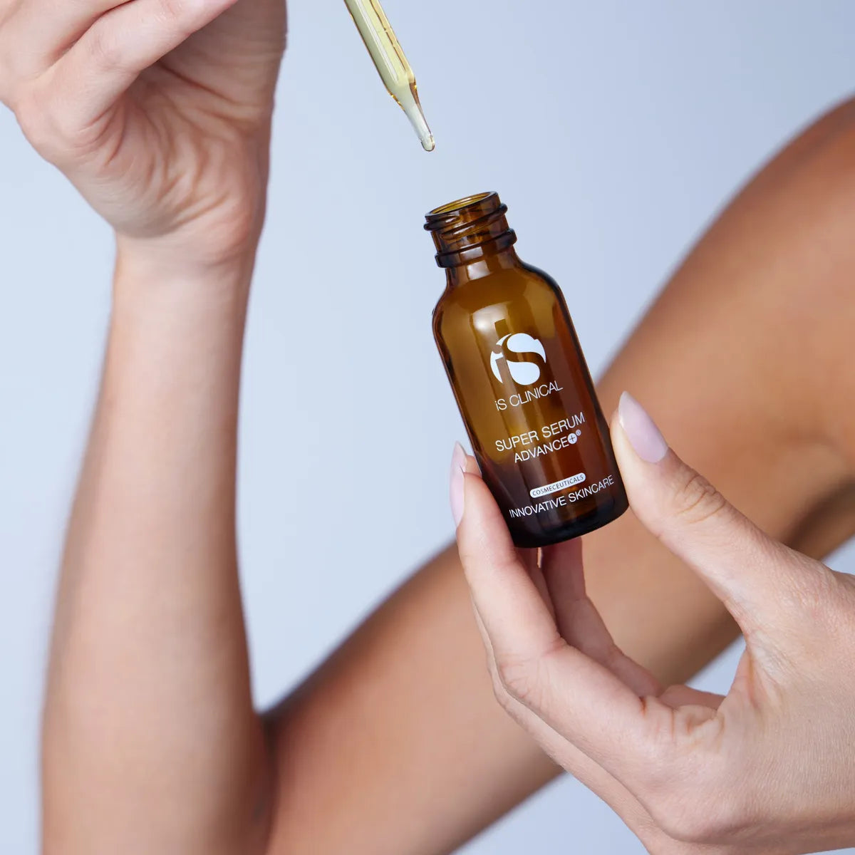 Hand holding a brown iS Clinical Super Serum Advance+ serum bottle with a dropper, against a light background